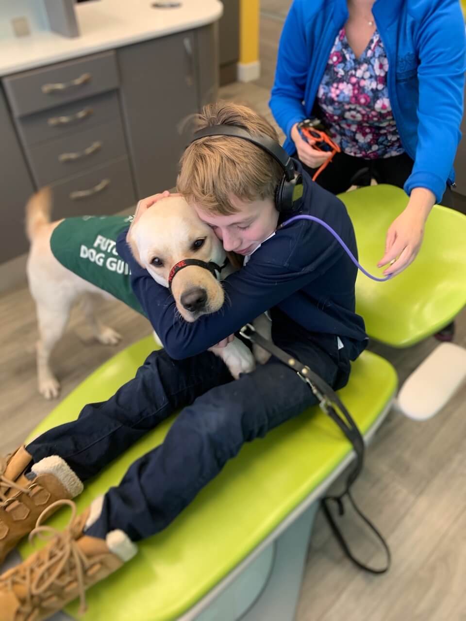 Child sitting in patient's chair, hugging a guide dog